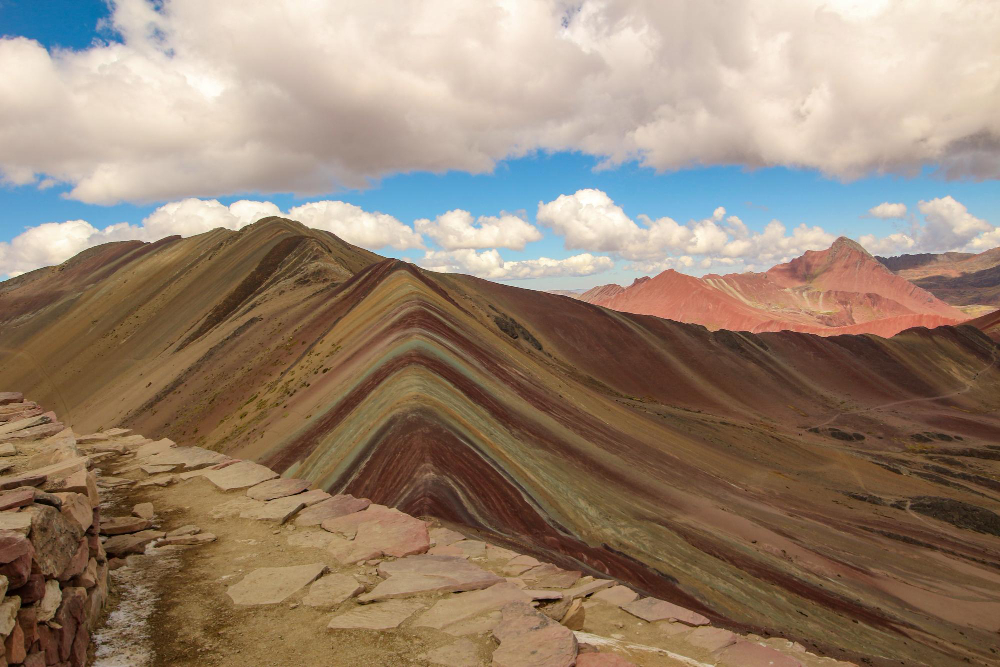 Rainbow Mountain (Vinicunca) in Peru, colorful striped Andes peaks near Cusco under a blue sky with clouds, high-altitude hiking trail.