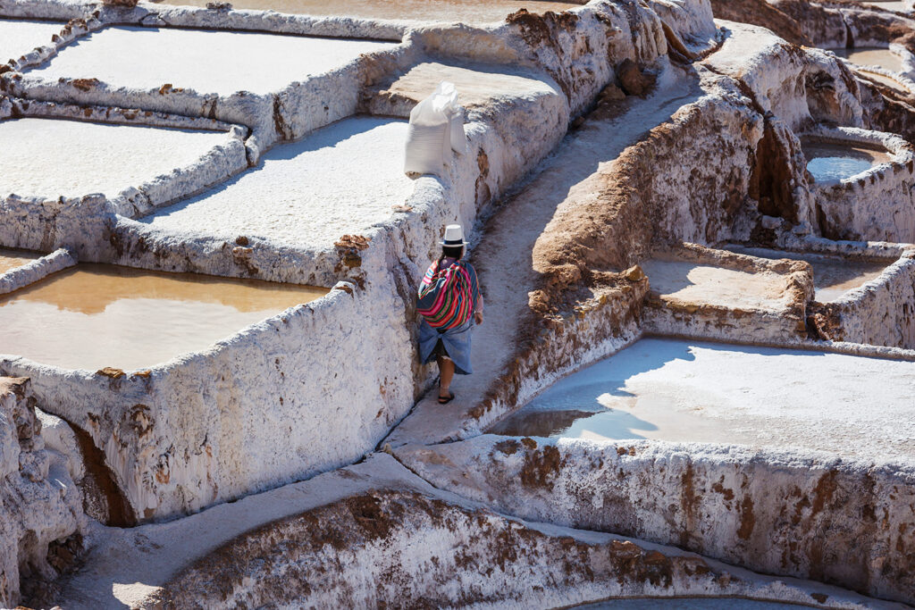 Local worker walking between white salt evaporation ponds at the Maras Salt Mines in Peru’s Sacred Valley.