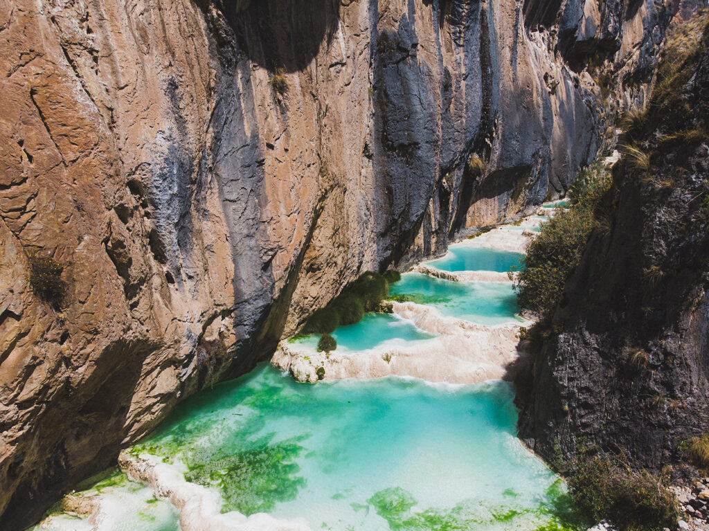 Close-up of Millpu’s turquoise waterfalls flowing between natural rock basins in the Peruvian Andes under clear sunlight.