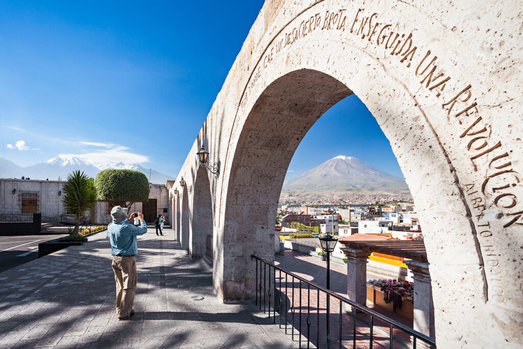 Traveler at the Yanahuara viewpoint in Arequipa, Peru, standing beneath white sillar arches with views over the city and Misti Volcano under a clear blue sky.